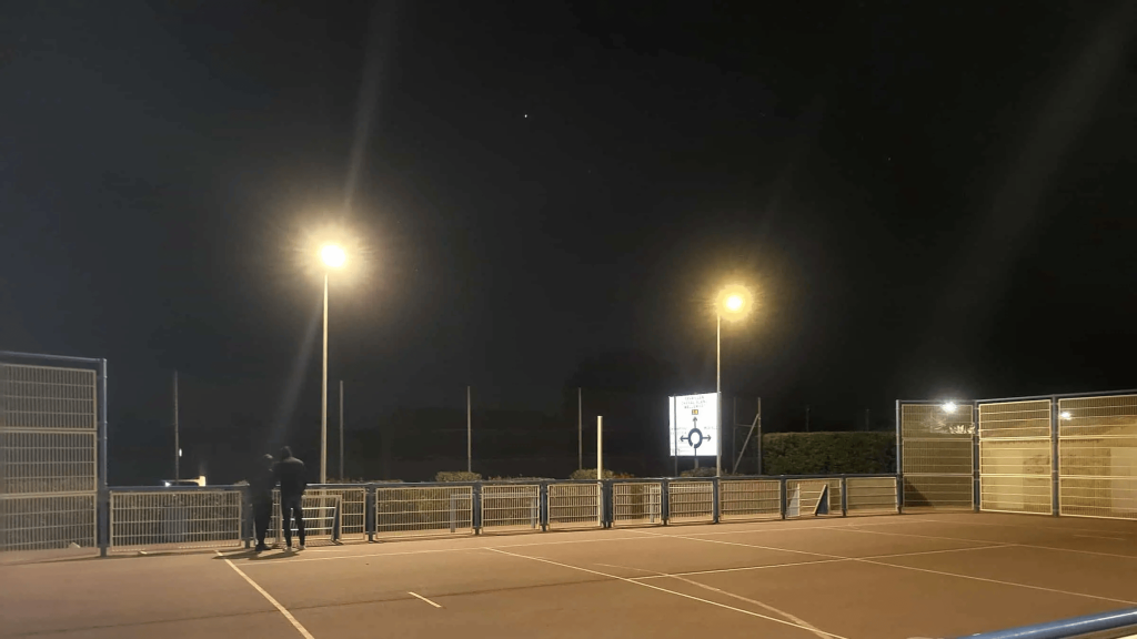 Two people near illuminated sports court.